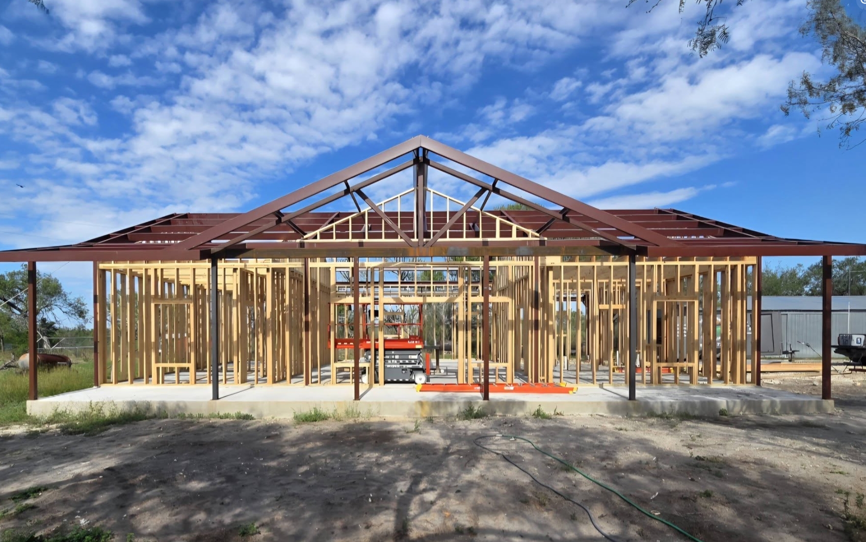Barndominium under construction, red steel frame over wood framing on a poured concrete slab