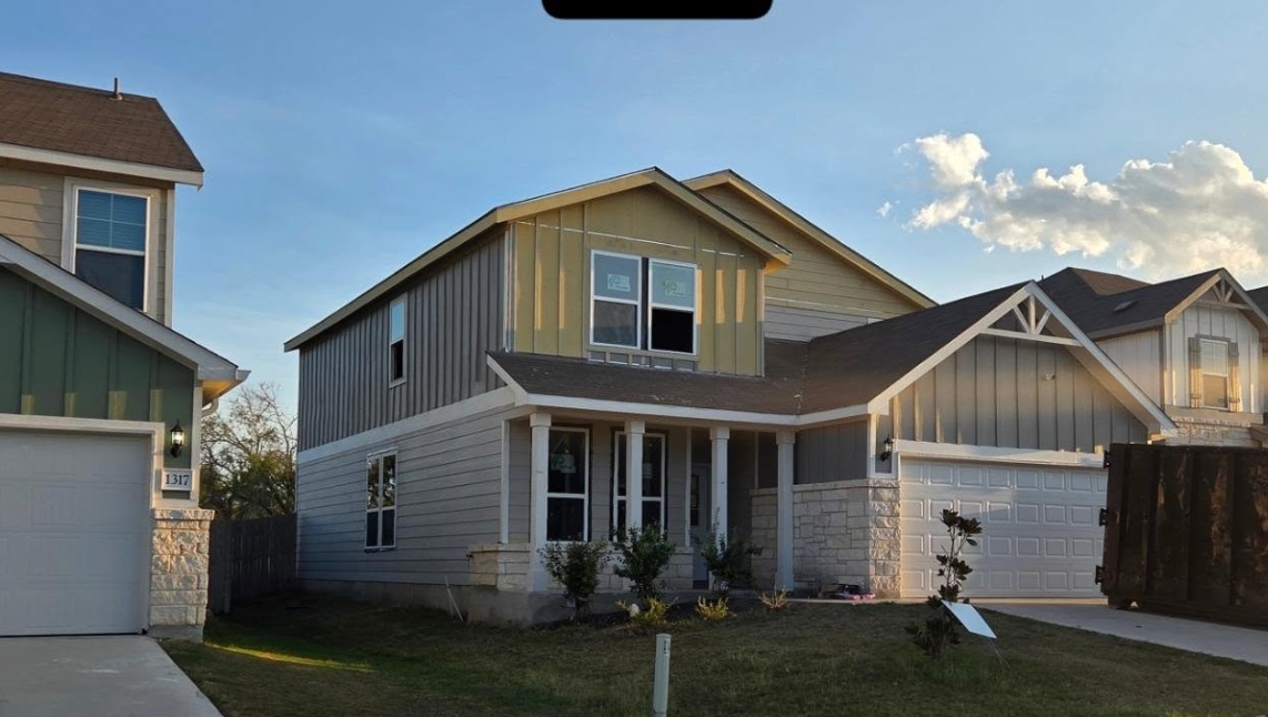The same home rebuilt — new roof on, fresh sheathing across the upper gable and siding going back up