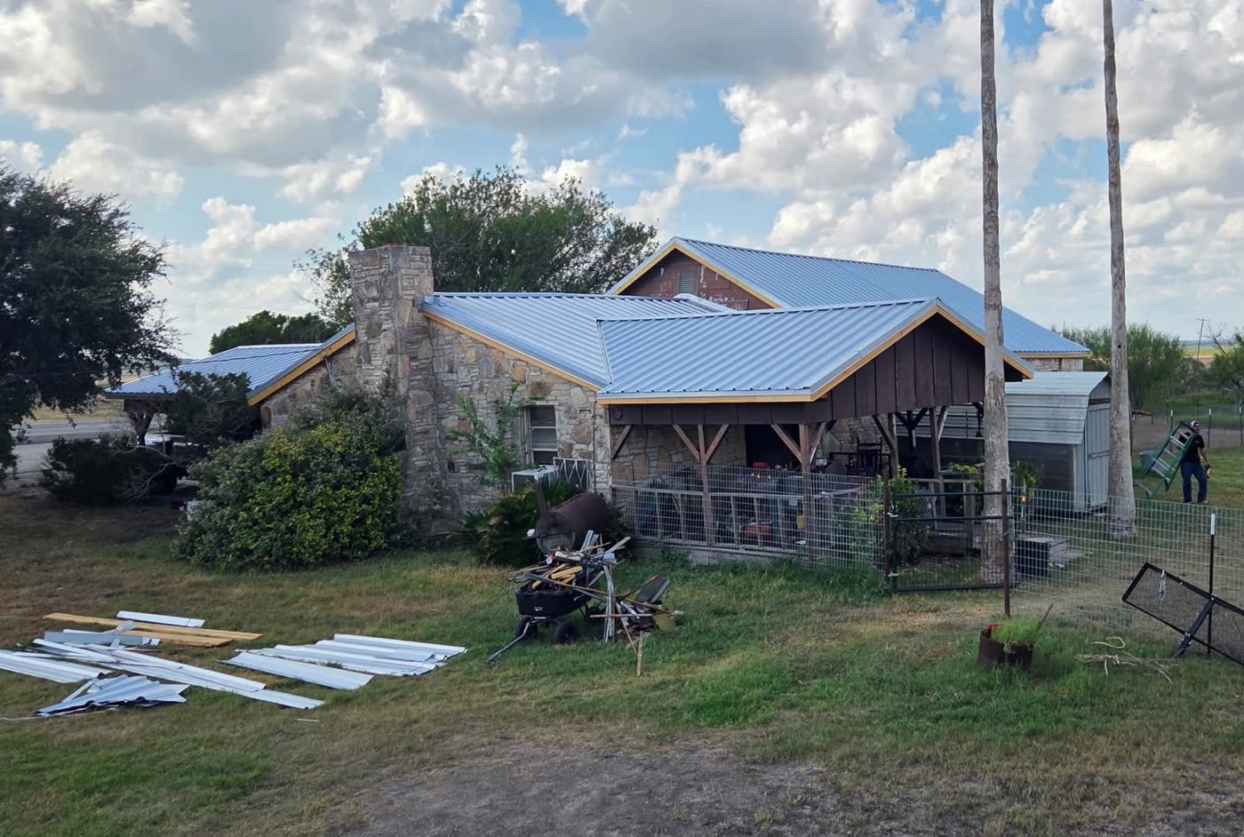 Stone ranch house with a brand new metal roof across the house, porch and carport, the old panels stacked on the grass below